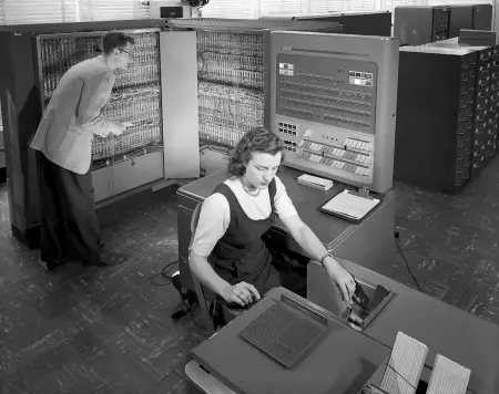 رجل وامرأة يعملان على حاسوب معالجة البيانات الإلكتروني IBM 704 المستخدم في إجراء الحسابات لأبحاث الطيران في لانغلي التابعة لوكالة ناسا (NACA).